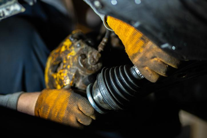 A mechanic examining a torn CV axle boot for grease leakage