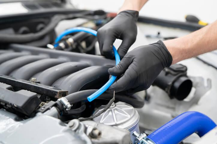 An automotive student checking a brake booster vacuum hose for leaks