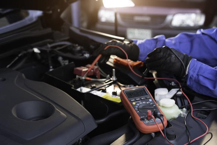 A student using a digital multimeter to test a vehicle charging system
