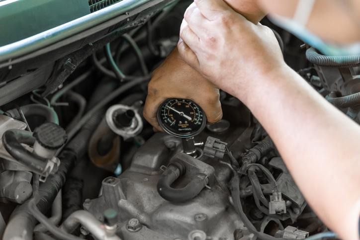 An automotive student performing a fuel pressure test on a vehicle