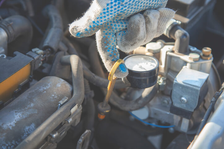 A technician checking engine oil pressure with a mechanical gauge