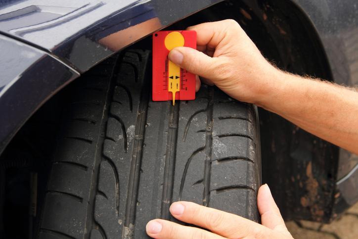 An automotive student checking AWD tire tread difference with a tread-depth gauge