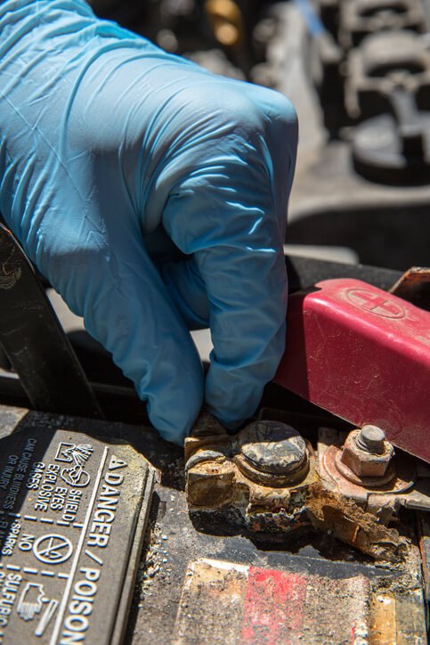 A technician checking corroded battery terminals during slow-crank diagnosis