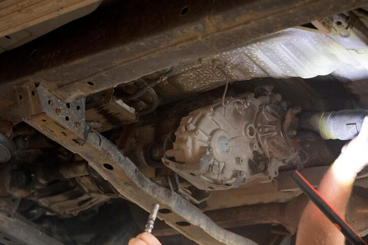 An automotive student checking transfer case fluid beneath a four-wheel-drive vehicle