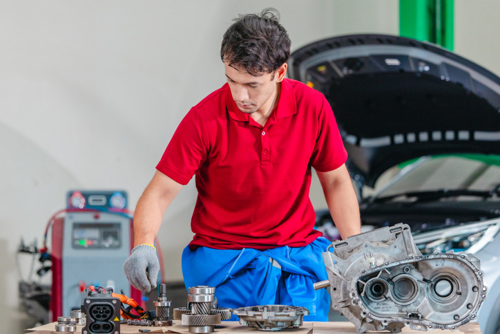 An automotive technician inspecting electrified drivetrain components with high-voltage cables.