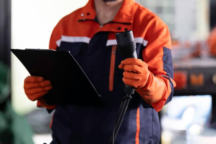 A technician checking an EV charge-port release mechanism during vehicle service