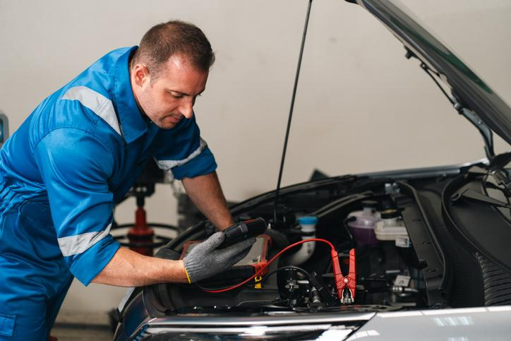 Automotive technician using a handheld diagnostic meter under a vehicle hood