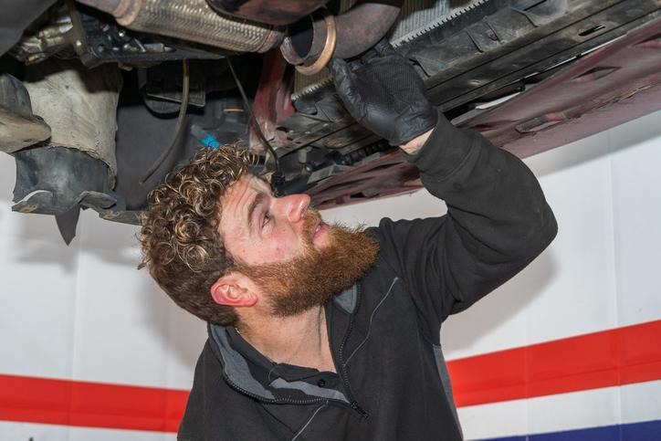 An automotive student inspecting an exhaust system for winter corrosion